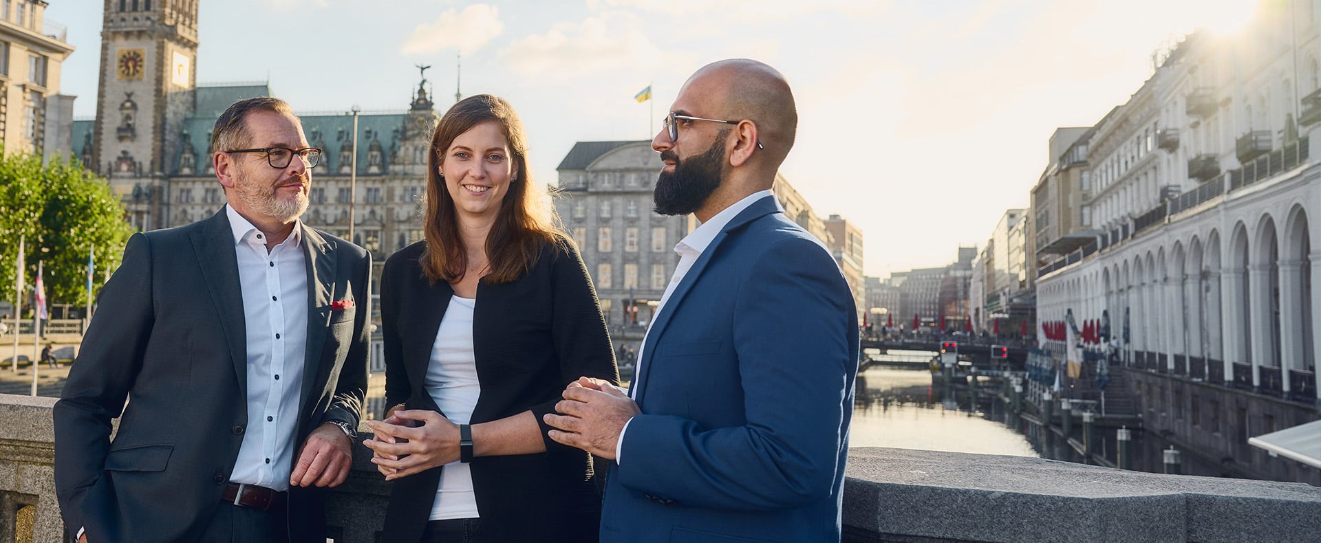 Zwei Männer und eine Frau stehen auf einer Brücke vor dem Hamburger Rathaus